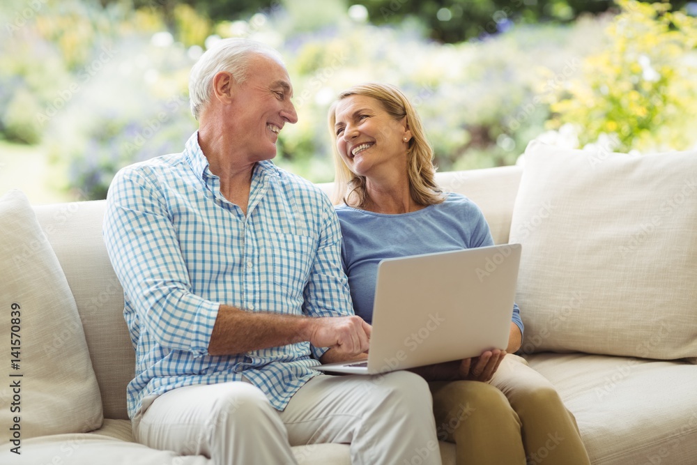 Fototapeta premium Senior couple interacting with each other while using laptop in living room