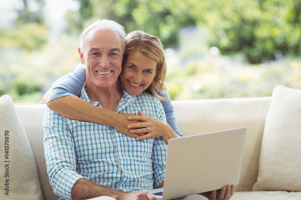 Portrait of smiling senior woman embracing a man in living room while using laptop Portrait of smiling senior woman embracing a man in living room while using laptop