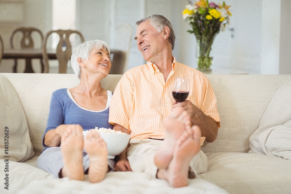Senior couple having popcorn and glass of wine in living room Senior couple having popcorn and glass of wine in living room