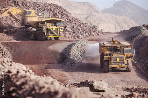 Loading of copper ore on very big dump-body truck and watering road tanker