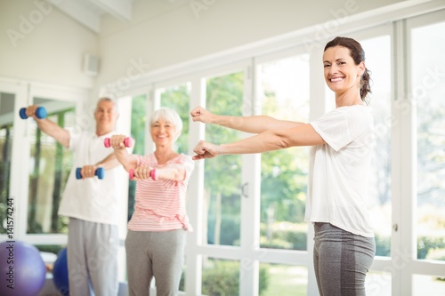 Female trainer assisting senior couple in performing exercise