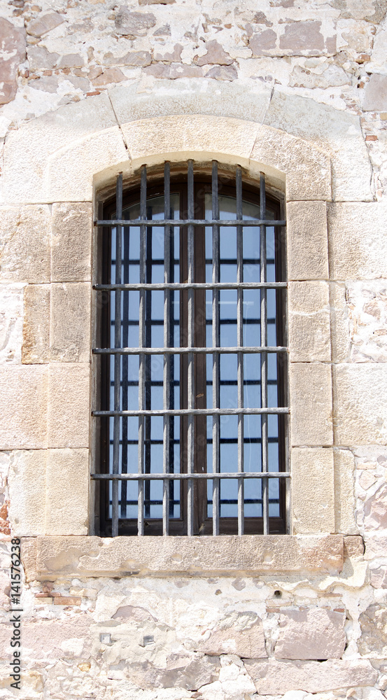 An ancient window with metal bars in an old fortification wall
