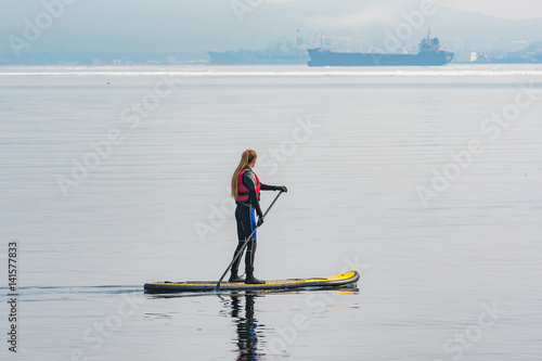 A girl is rolling on the sea on a soup board. Young blonde female paddles a paddleboard at the sea. 