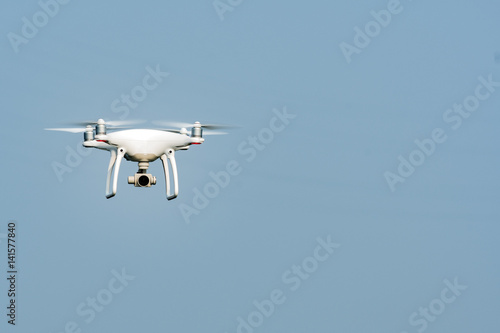 White drone, quadrocopter, with photo camera flying in the blue sky. Drone fly in the blue sky