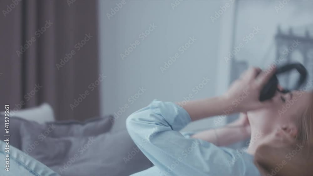 Young Caucasian teen girl putting on headphones on a sofa at home and enjoying music from a vinyl turntable. 4K UHD RAW edited footage Young Caucasian teen girl putting on headphones on a sofa at home and enjoying music from a vinyl turntable. 4K UHD RAW edited footage