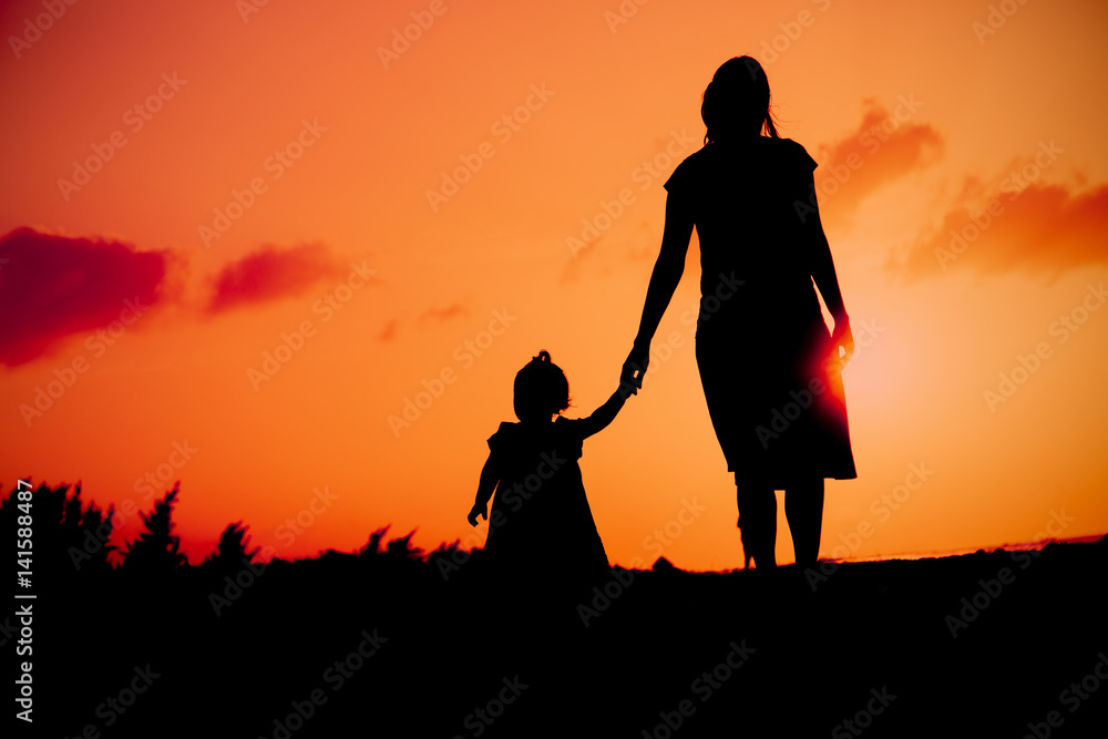 Silhouette of mother and daughter walking on beach at sunset