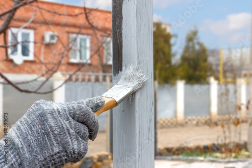 Hand in rag glove paint brush steel post in gray anti rust paint  on a background of house.  Half - painted surface. Smear of paint brush.
