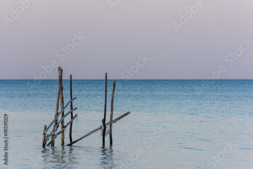 A frame made from old wooden posts stands in a calm sea at golden hour.