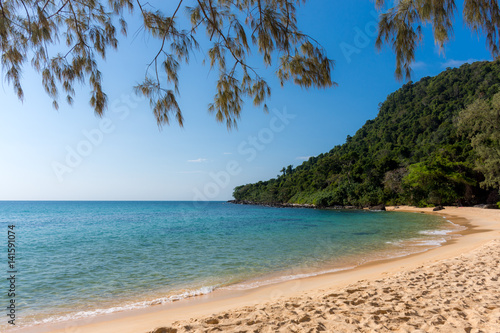 White sandy beach bay with forested headland in the distance on a tropical island.