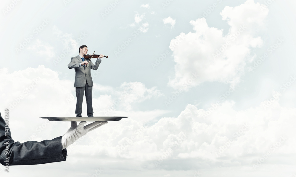 Businessman on metal tray playing violin against blue sky background Businessman on metal tray playing violin against blue sky background