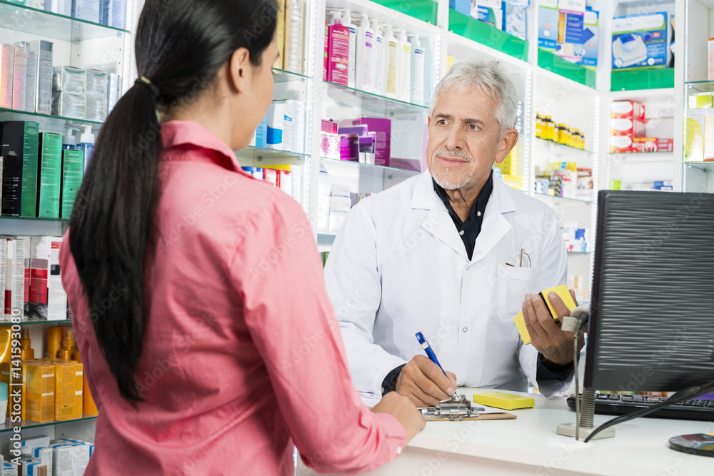 Pharmacist Writing On Clipboard While Looking At Woman
