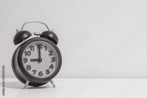 Closeup alarm clock for decorate in 9 o'clock on white wood desk and cream wallpaper textured background in black and white tone with copy space