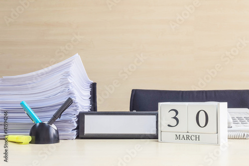 Closeup white wooden calendar with black 30 march word on blurred brown wood desk and wood wall textured background in office room view with copy space , selective focus at the calendar