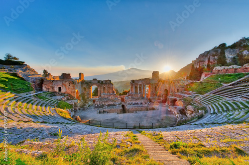 Ancient theatre of Taormina with Etna erupting volcano at sunset photo