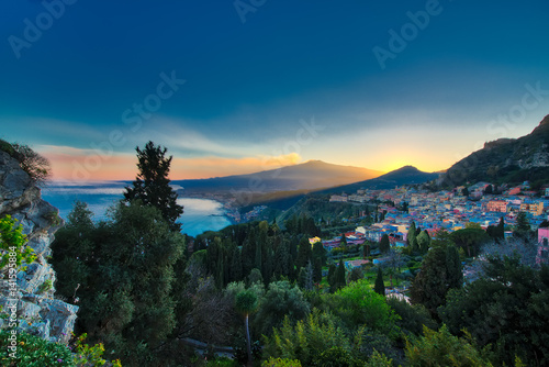 View of Taormina in Sicily at sunset with the Etna volcano erupting