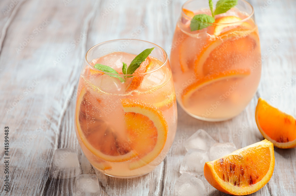 Cold refreshing drink with blood orange slices in a glass on a wooden background. Selective focus, copy space. Cold refreshing drink with blood orange slices in a glass on a wooden background. Selective focus, copy space.