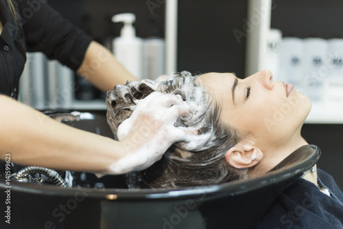 Beautiful young woman with hairdresser washing head at hair salon