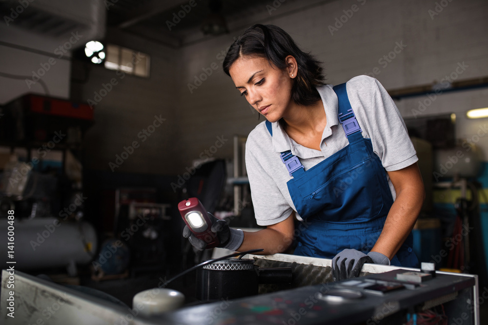 female mechanic looking for a fault on a compressor engine using a flashlight female mechanic looking for a fault on a compressor engine using a flashlight
