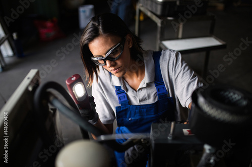 female mechanic looking for a fault on a compressor engine using a flashlight