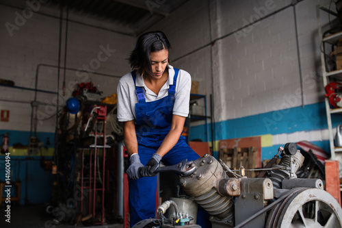 female mechanic fixing a compressor enginge using a wrench photo