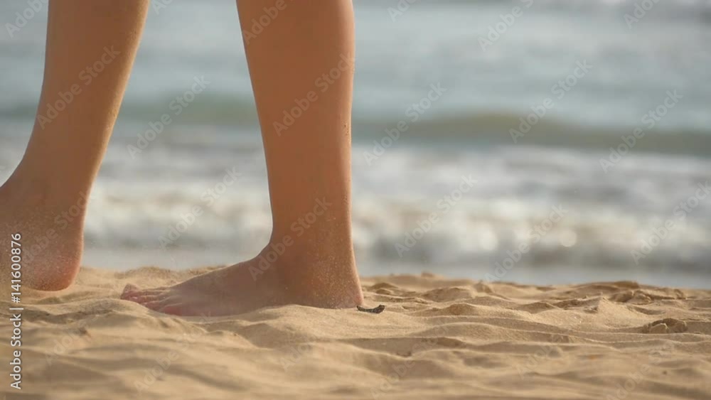 Close up of female feet walking on golden sand at the beach with ocean waves at background. Legs of young woman stepping at sand. Barefoot girl at the sea shore. Summer vacation holiday. Slow motion Close up of female feet walking on golden sand at the beach with ocean waves at background. Legs of young woman stepping at sand. Barefoot girl at the sea shore. Summer vacation holiday. Slow motion