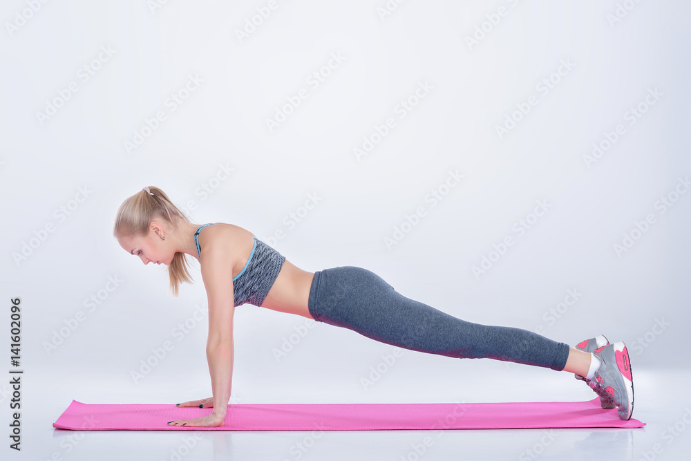 beautiful blonde girl in sportswear does exercises on fitness Mat on gray background beautiful blonde girl in sportswear does exercises on fitness Mat on gray background