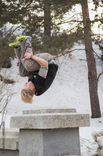 Teenager blonde hair man training parkour jump in the snow covered park photo