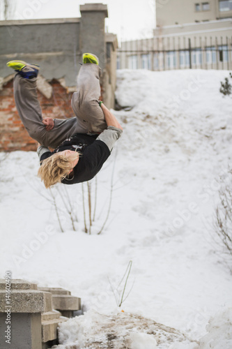 Teenager blonde hair guy training parkour jump flip in the snow covered park photo