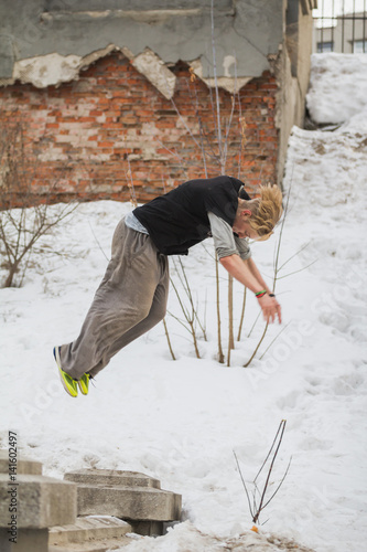 Free-run work out - teenager blonde hair guy training parkour jump flip in the snow covered park photo