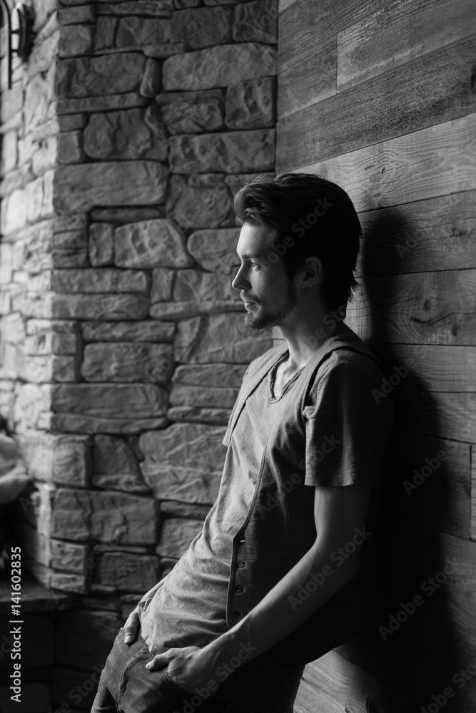 Black and white side view of stylish young man leaning on wall indoor Black and white side view of stylish young man leaning on wall indoor