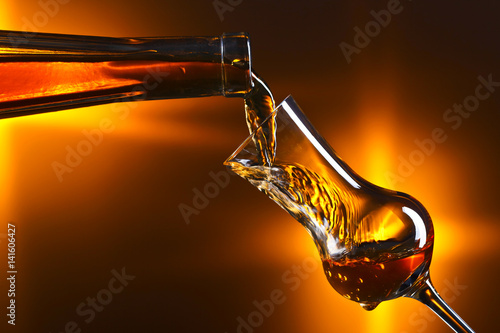 Canvas Print Pouring alcohol into a glass on dark background