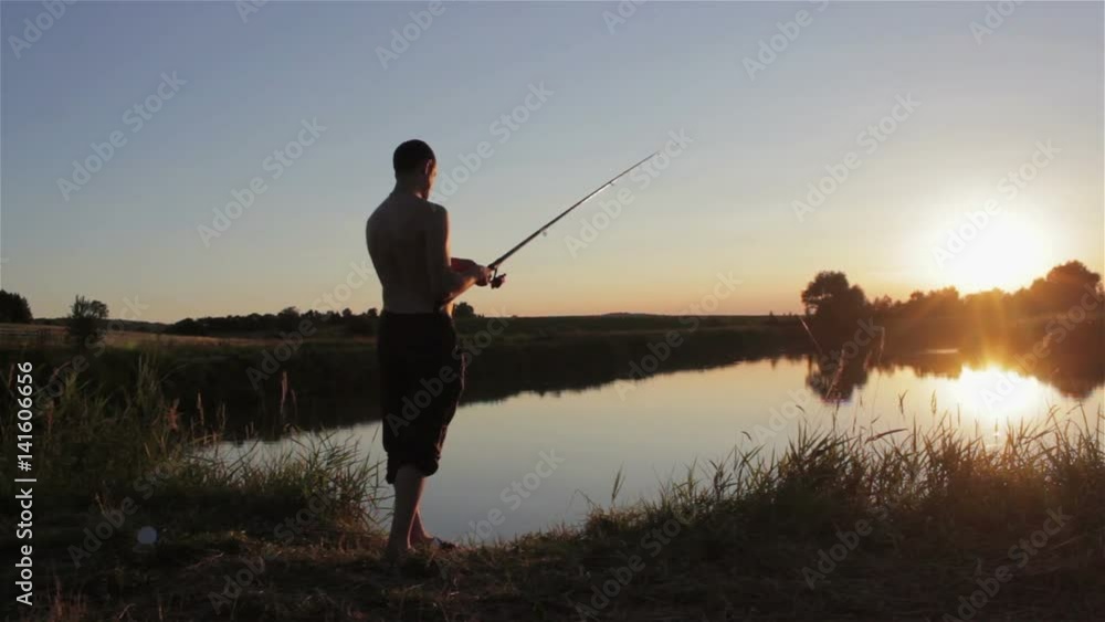 Man Fishes With Spinning At Sunset/man standing on the lake at sunset with fishing rod Man Fishes With Spinning At Sunset/man standing on the lake at sunset with fishing rod