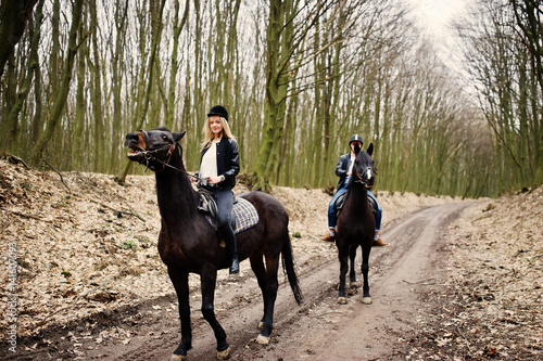 Young stylish couple riding on horses at autumn forest.