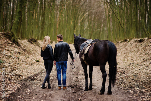 Back of young stylish couple in love walking with horse at autumn forest.