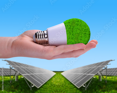 Eco LED bulb in hand in the background solar energy panels. The concept of sustainable resources.