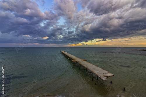 old broken bridge in the sea at cloudy sunset