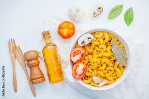 Italian foods concept and menu design . Pasta elbow macaroni with ingredients sweet basil ,tomato ,garlic ,extra virgin olive oil ,parsley ,bay leaves and champignon on white background flat lay .