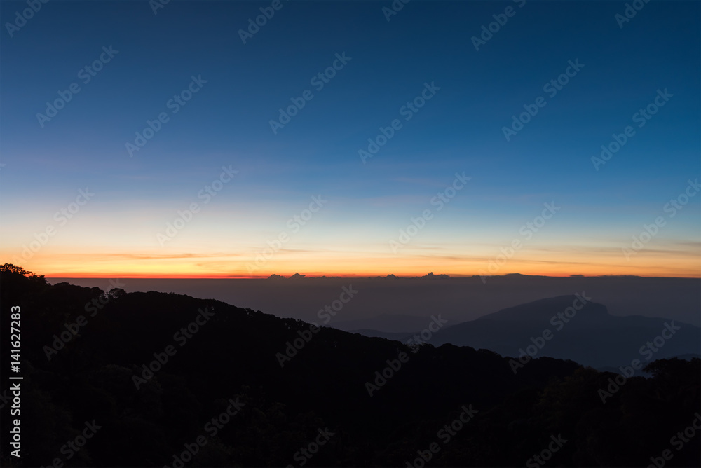 Twilight on clear sky before sunrise over dark mountains in shadow.