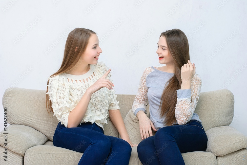 Three happy friends talking and drinking coffee and tea sitting on a couch at home