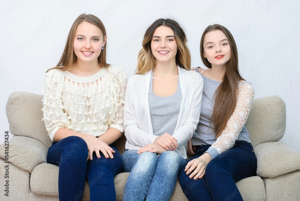 © Saksoni - Three happy friends talking and drinking coffee and tea sitting on a couch at home