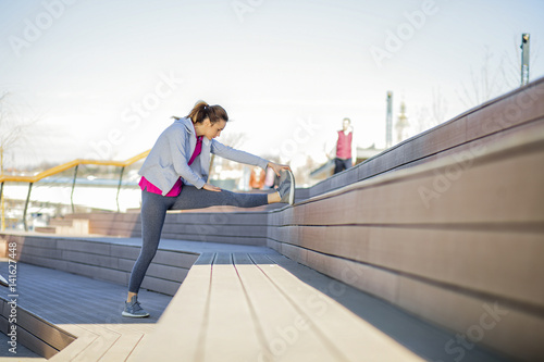 Fototapeta Naklejka Na Ścianę i Meble -  Morning exercise near the river. Young woman on recreation and jogging.
Warm up and stretch muscles before the morning exercise by the river