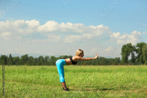 Beautiful sport woman doing stretching fitness exercise in city park at green grass. Yoga postures © Igor
