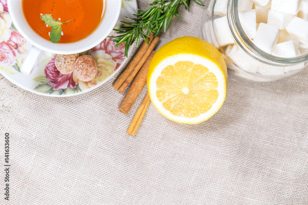 Cup of black or red tea with lemon, rosemary, mint, cinnamon sticks, sugar on grey tablecloth, top view