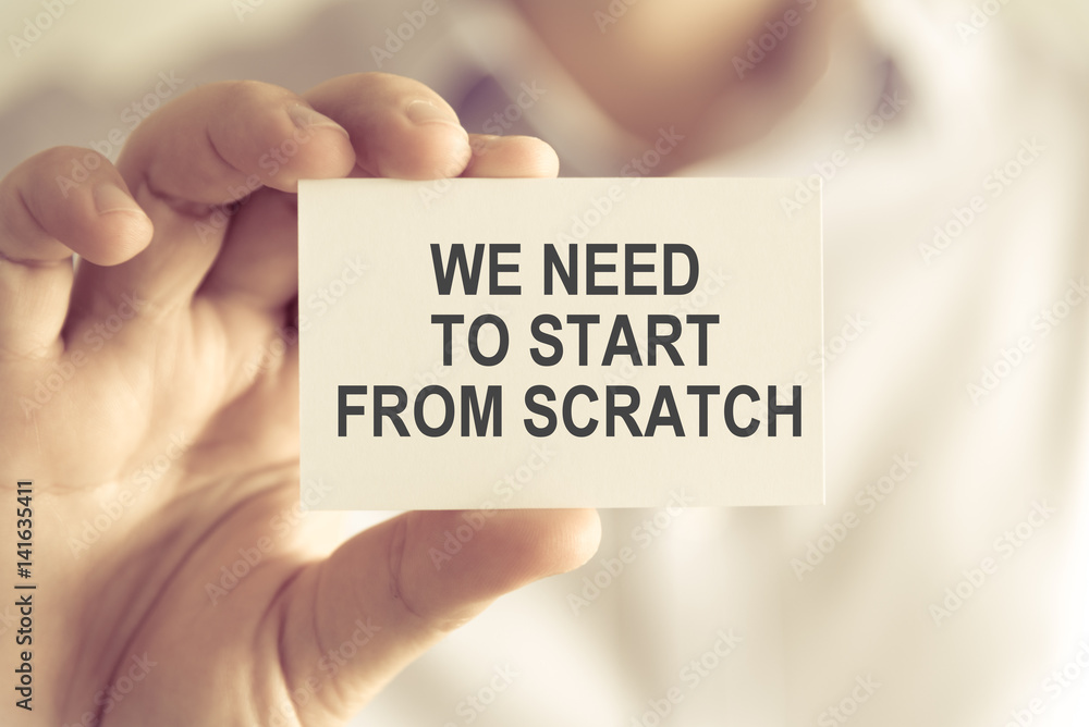 Businessman holding WE NEED TO START FROM THE SCRATCH message card Businessman holding WE NEED TO START FROM THE SCRATCH message card