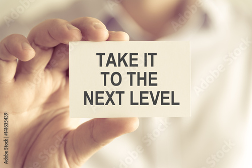 Businessman holding TAKE IT TO THE NEXT LEVEL message card