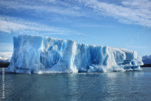 Single big blue iceberg in blue water in the center of the picture and blue sky with clouds on the background. Patagonia, Argentina