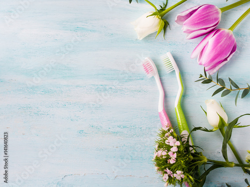 Two pastel toothbrushes with flowers herbs over green textured background. Spring colors. Personal dental health care. Healthy couple concept