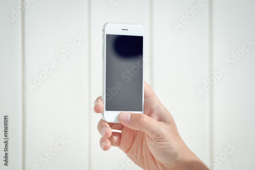 Hand holding mobile phone on wooden background. Closeup copy space