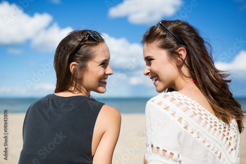 Two beautiful women on beach looking at each other laughing