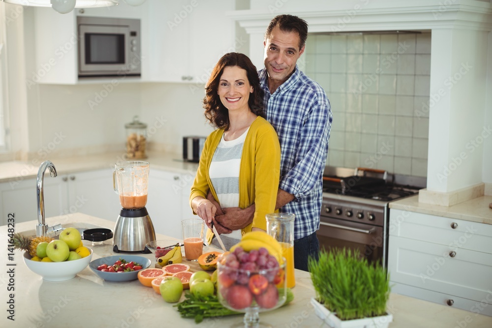 Happy couple embracing while preparing smoothie in kitchen Happy couple embracing while preparing smoothie in kitchen